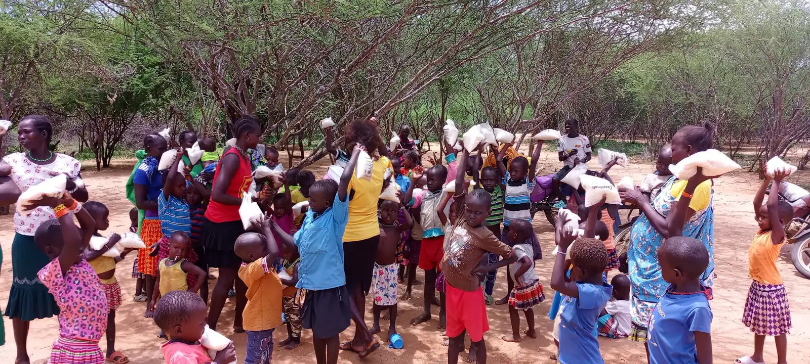 Families gathered under the thorn trees at a food distribution